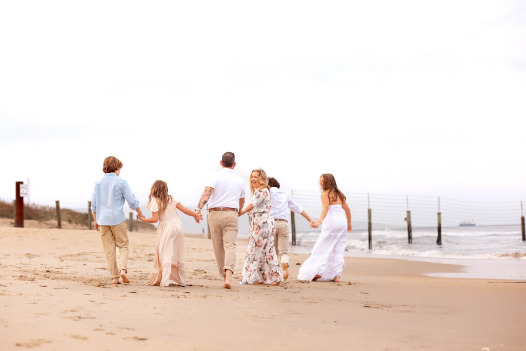 family dressed in colorful pastels walks together hand in hand on the beach in virginia beach