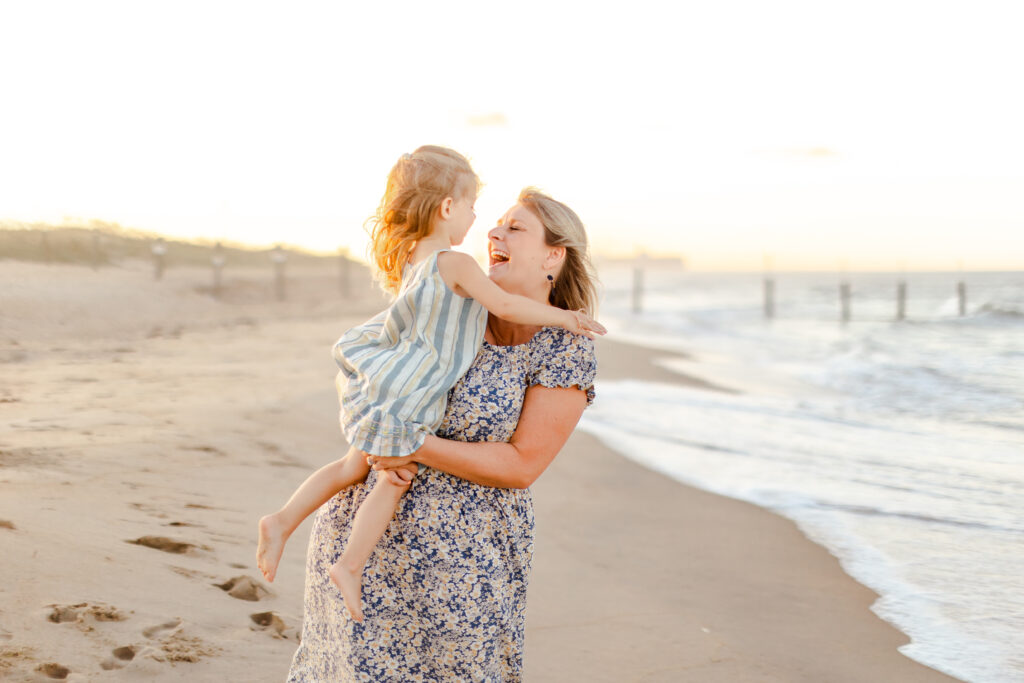 sun drenched mother and daughter laugh while twirling during a joy filled play centered family photo shoot in virginia beach