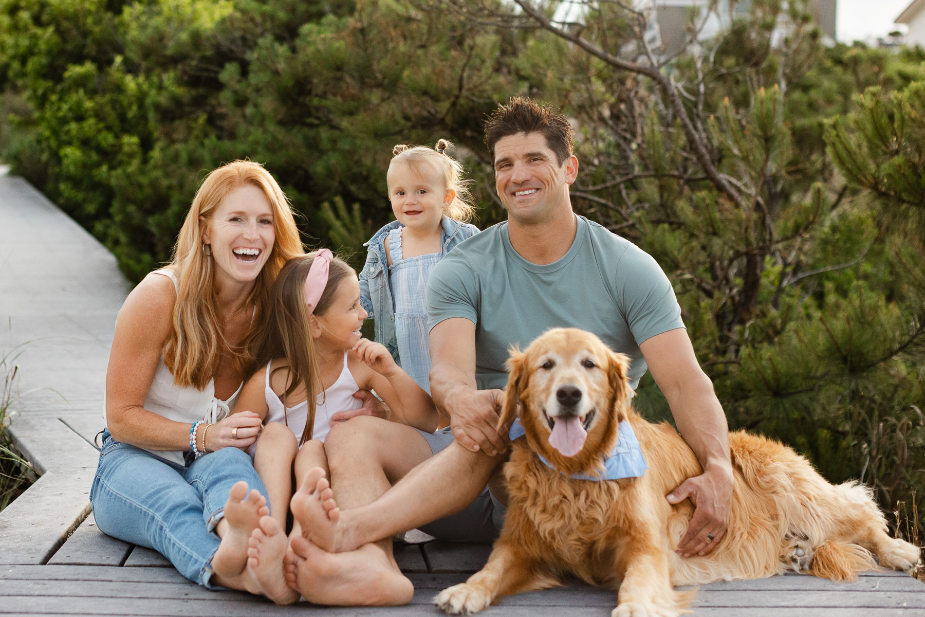 A family of four and their golden retriever laughing and play together on a boardwalk in Virginia Beach